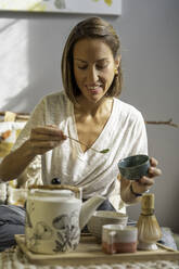 Girl making matcha tea on her couch at home - CAVF69519