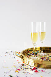 Champagnerflöten im Tablett mit Konfetti auf dem Tisch vor weißem Hintergrund - CAVF69625