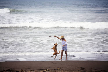 Glückliche Frau spielt mit Hund am Strand - CAVF69658