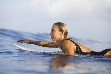 Confident woman lying on surfboard at beach against sky - CAVF69675