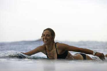 Portrait of happy woman lying on surfboard at beach against sky - CAVF69681