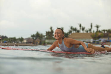 Lächelnde Frau auf einem Surfbrett im Meer liegend gegen den Himmel - CAVF69684