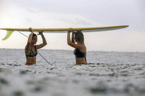 Freunde tragen Surfbrett auf dem Kopf im Meer während der Regenzeit - CAVF69686