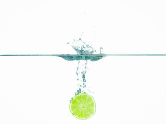 Lime slice in water against white background - CAVF69708
