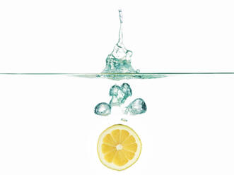Zitronenscheibe in Wasser vor weißem Hintergrund - CAVF69714