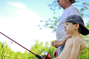 Side view of boy with grandfather fishing against sky - CAVF69735