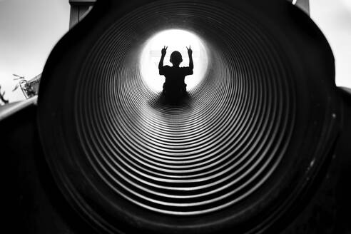 Silhouette Junge gestikuliert, während er auf einer Tunnelrutsche rutscht - CAVF69737