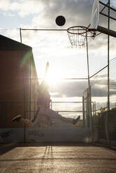 Teenager playing basketball, dunking against the sun - CJMF00188