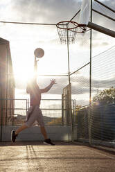 Teenager playing basketball, dunking against the sun - CJMF00189