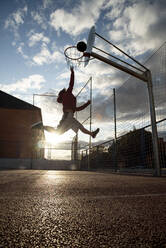 Teenager playing basketball, dunking against the sun - CJMF00190