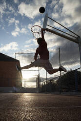 Teenager playing basketball, dunking against the sun - CJMF00191