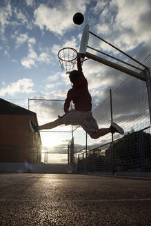 Jugendlicher spielt Basketball und dunkt gegen die Sonne - CJMF00191