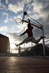 Teenager playing basketball, dunking against the sun - CJMF00192
