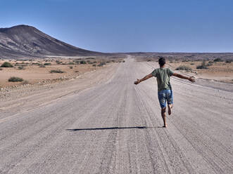 Mann läuft frei auf einer endlosen Straße, Rückansicht, Damaraland, Namibia - VEGF00999