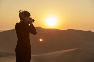 Woman taking a picture of the desert at sunset, Dune 7, Namibia - VEGF01000