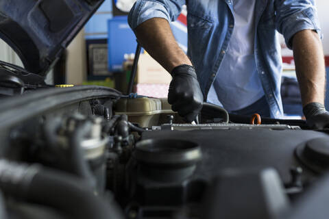 Mann in Hemd und Handschuhen arbeitet in einer Autowerkstatt und repariert einen Automotor, lizenzfreies Stockfoto