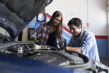 Ein fröhlicher Mann und eine junge Frau arbeiten zusammen an einer Autoreparatur und reparieren einen Automotor - ABZF02856