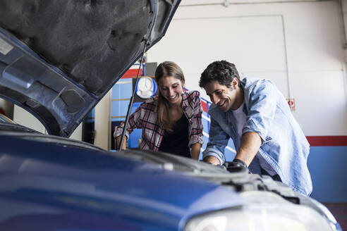 Ein fröhlicher Mann und eine junge Frau arbeiten gemeinsam an einer Autoreparatur und reparieren gemeinsam den Motor eines Autos - ABZF02857