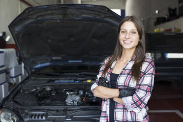 Casual woman in checkered shirt and gloves holding arms crossed and smiling at camera, working in car service - ABZF02862