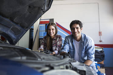 Junge Frau und Mann stehen in der Nähe von Auto in Service-Center lächelnd in die Kamera und arbeiten im Team - ABZF02864