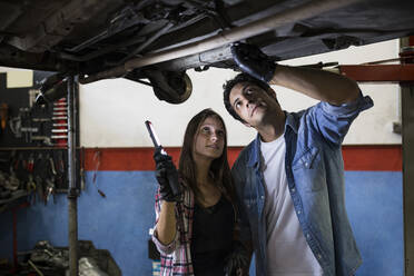 Man and woman with torch standing under car on leveling jack and exploring bottom working in service center in Madrid - ABZF02871