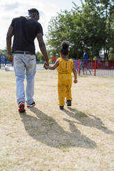 Rückansicht von Vater und Tochter, die Hand in Hand in einem Park spazieren gehen - FBAF01003