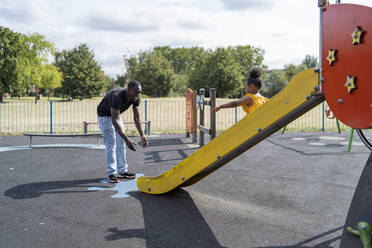 Vater mit Tochter rutscht auf einem Spielplatz - FBAF01005