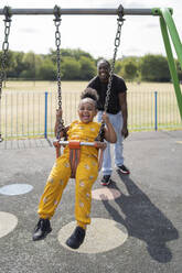 Father with happy daughter swinging on a playground - FBAF01014