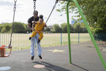 Vater mit glücklicher Tochter beim Schaukeln auf einem Spielplatz - FBAF01016