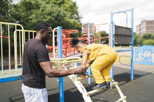 Father helping daughter climbing up a ladder on a playground - FBAF01023