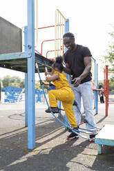 Vater hilft Tochter auf einem Spielplatz auf eine Strickleiter - FBAF01029