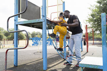 Vater hilft Tochter auf einem Spielplatz auf eine Strickleiter - FBAF01030