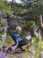 Man in garden reading newspaper - JOHF04661