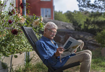 Man in garden reading newspaper - JOHF04662
