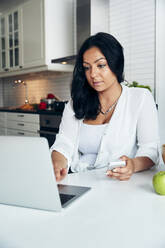 Woman using laptop in kitchen - JOHF04720