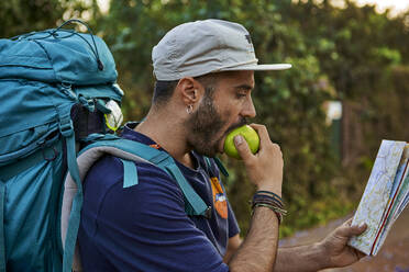 Backpacker biting an apple and checking his map - VEGF01010