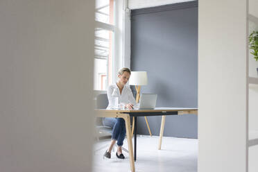 Junge Geschäftsfrau mit Laptop am Schreibtisch im Büro - MOEF02644