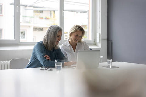 Two businesswomen using laptop at desk in office together stock photo