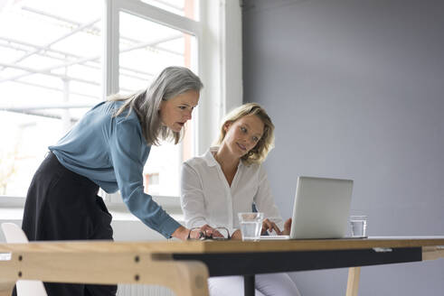 Zwei Geschäftsfrauen benutzen gemeinsam einen Laptop am Schreibtisch im Büro - MOEF02662