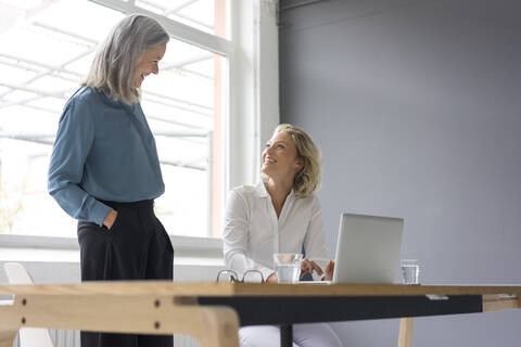 Zwei Geschäftsfrauen lächeln sich am Schreibtisch im Büro gegenseitig an, lizenzfreies Stockfoto