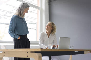 Zwei Geschäftsfrauen lächeln sich am Schreibtisch im Büro gegenseitig an - MOEF02663