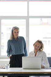 Zwei Geschäftsfrauen benutzen gemeinsam einen Laptop am Schreibtisch im Büro - MOEF02664