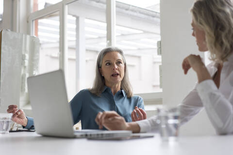 Zwei Geschäftsfrauen diskutieren am Schreibtisch im Büro, lizenzfreies Stockfoto