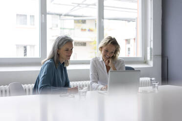 Zwei Geschäftsfrauen benutzen gemeinsam einen Laptop am Schreibtisch im Büro - MOEF02669