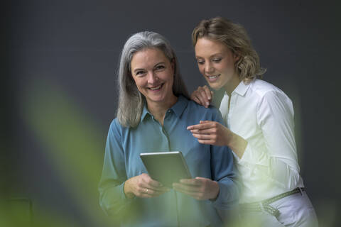 Zwei lächelnde Geschäftsfrauen teilen sich ein Tablet, lizenzfreies Stockfoto