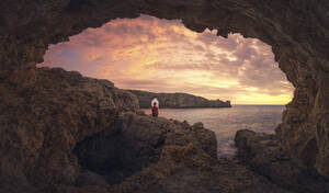 Rückansicht eines Mannes, der bei Sonnenuntergang in einer Höhle sitzt, Menorca, Spanien - DVGF00070