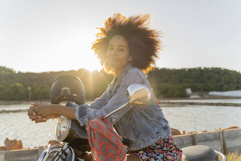 Junge Frau sitzt auf einem Motorroller bei Sonnenuntergang, Ibiza, lizenzfreies Stockfoto