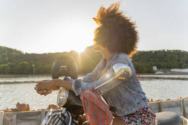 Young woman sitting on motor scooter at sunset, Ibiza - AFVF04357