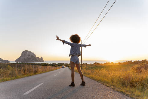 Junge Frau steht bei Sonnenuntergang auf der Straße, Ibiza - AFVF04367