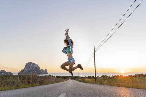 Junge Frau springt bei Sonnenuntergang auf die Straße, Ibiza - AFVF04373